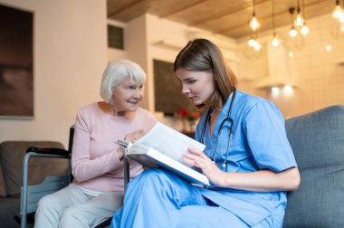 Birlikte okuyoruz. Yaşlı bir bayana kitap okuyan bir kadın bakıcı.