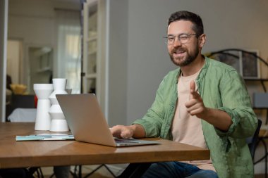 Masada oturan bir iş adamı dizüstü bilgisayarda başparmağını bir jest gibi gösteriyor.