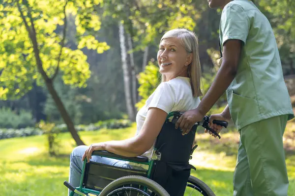 Parkta. Parkta tekerlekli sandalyede bir kadın hasta ile hemşire.