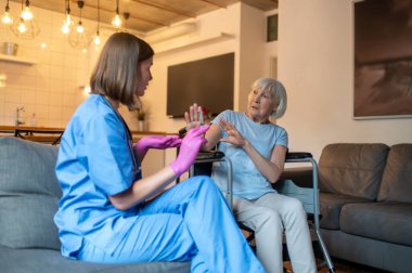 İğnelerin kutsallığı. Üniformalı hemşire iğneye ilaç hazırlıyor, yaşlı hasta korkmuş görünüyor.