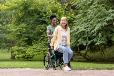 İyileşme. Afrikalı Amerikalı hemşire, parkta tekerlekli sandalyeyle kadın hasta gezdiriyor.
