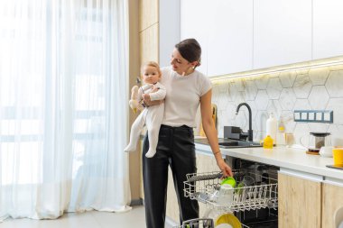 Oğlu ve annesi. Genç baba oğlunu tutarken tabakları çamaşır makinesine koyuyor.
