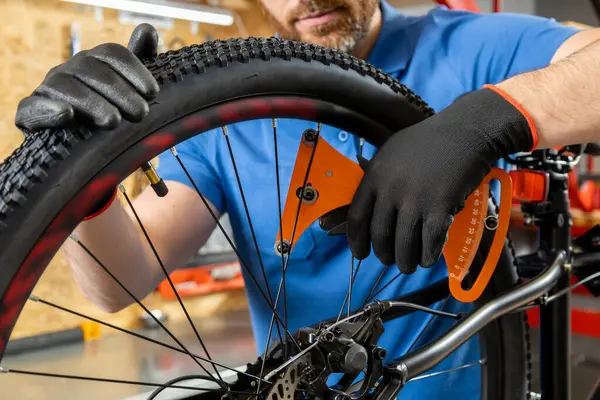 Tamircinin elleri atölye ortamında turuncu bir aletle bisiklet tekerleğini manipüle ediyor.
