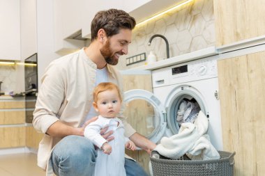 Ev işi. Genç adam ve küçük oğlu çamaşır makinesine koymadan önce elbiselerini ayırıyorlar.