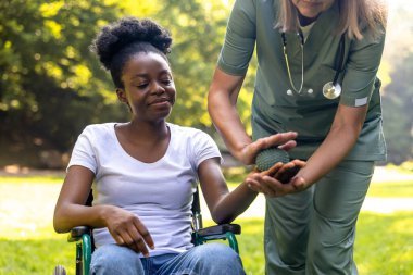 Rehabilitasyon. Parkta Afrikalı Amerikalı bir kadın hastayla rehabilitasyon egzersizleri yapan hemşire.