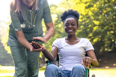 Rehabilitasyon. Parkta Afrikalı Amerikalı bir kadın hastayla rehabilitasyon egzersizleri yapan hemşire.