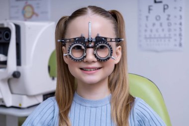 Optometri. Açık renk saçlı okul kızı klinikte optometri testi yaptırıyor.