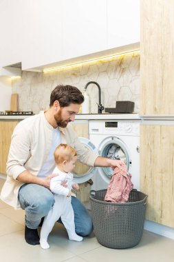 Ev işi. Genç adam ve küçük oğlu çamaşır makinesine koymadan önce elbiselerini ayırıyorlar.