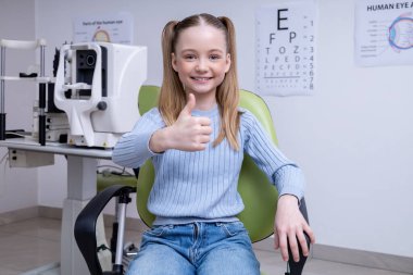 Doktoru ziyaret et. Gülümseyen tatlı kız göz doktorunun ofisinde oturuyor ve mutlu görünüyor.