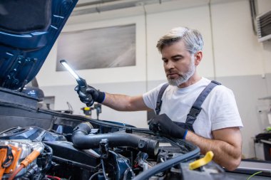 Tamircide kaputu açık motoru incelemek için el feneri kullanan bir tamirci.