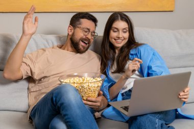 Mutlu çift, kanepede patlamış mısırla evde oturup film izlemenin keyfini çıkarıyor.