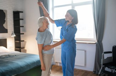 Egzersiz yapıyorum. Yaşlı bayan bir eğitmenle egzersiz yapıyor ve ilgili görünüyor.