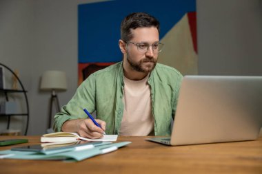 İç işlerinde bilgisayar ve kağıtlarla çalışırken masadaki notları inceleyen sakallı adam.