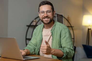 Masada oturan bir iş adamı dizüstü bilgisayarda başparmağını bir jest gibi gösteriyor.