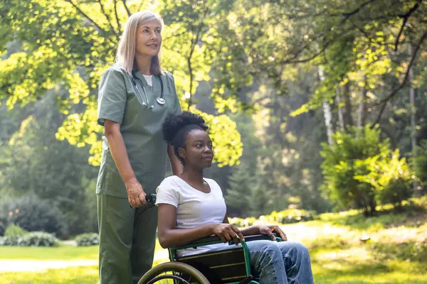 Rehabilitasyon merkezi. Parkta tekerlekli sandalyede bir hemşire ve bir kadın.