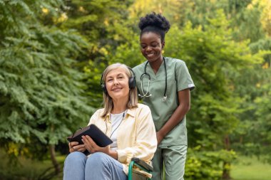 Sabah yürüyüşü. Tekerlekli sandalyedeki kadın ve hemşire parkta yürüyor.