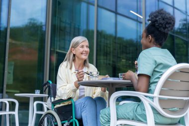 Öğle yemeği vakti. Hemşire ve bayan hasta kliniğin bahçesinde yemek yiyorlar ve ilgili görünüyorlar.
