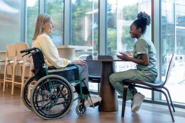 Destek ve bakım. Doktor ve hasta tekerlekli sandalyede konuşuyor ve huzurlu görünüyorlar.