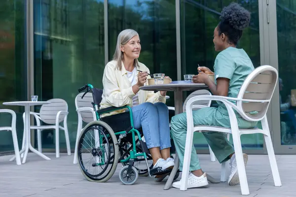Öğle yemeği vakti. Hemşire ve bayan hasta kliniğin bahçesinde yemek yiyorlar ve ilgili görünüyorlar.