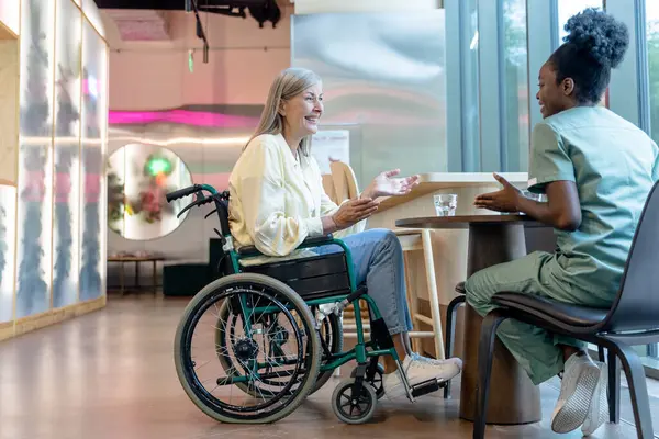Destek ve bakım. Doktor ve hasta tekerlekli sandalyede konuşuyor ve huzurlu görünüyorlar.