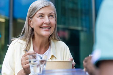 Öğle yemeği vakti. Hemşire ve tekerlekli sandalyede bir hasta birlikte yemek yiyor ve sohbet ediyorlar.