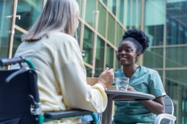 Öğle yemeği vakti. Hemşire ve bayan hasta kliniğin bahçesinde yemek yiyorlar ve ilgili görünüyorlar.