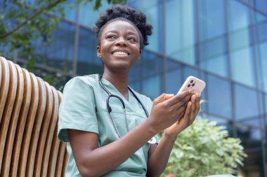 Kahve zamanı. Genç gülümseyen Afrikalı Amerikalı kadın laboratuvar önlüklü bankta oturuyor ve kahve içiyor.