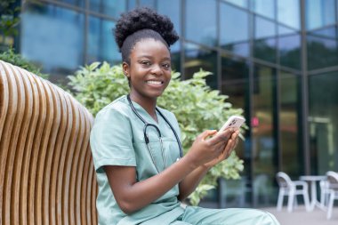 Telefon var. Elinde telefonla bankta oturan güzel gülümseyen bir bayan doktor.