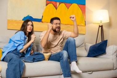 Heyecanlı çift modern kanepede oturup şov izliyor ya da TV 'de spor maçı izliyor. Yumruklar havada duygusal tepki veriyor.