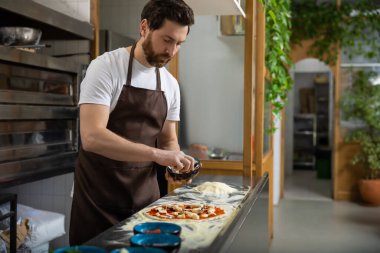 Adam mutfağa pizza malzemesi ekliyor. İçerde yemek hazırlıyor.