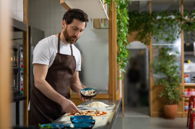 Adam mutfakta pizza hazırlıyor hamuru dikkatlice şekillendiriyor içeride yemek yapıyor.