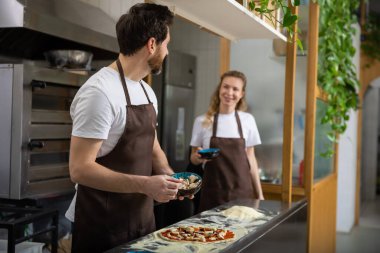 Adam mutfağa soslu pizza yayıyor ve içeride düzgün bir şekilde yemek hazırlıyor.