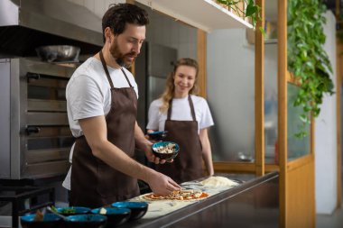 Erkek, kadın pizzasına mutfakta yardım eder ve evde mutlu bir şekilde yemek hazırlar.