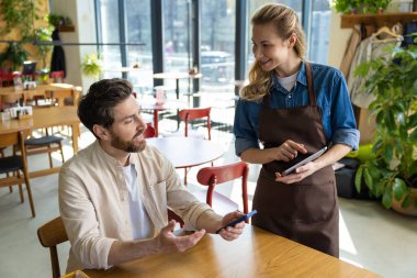 Garson, lokantadaki tablete sipariş veriyor. İçerideki adam telefonu kontrol ederken verimli bir şekilde çalışıyor.