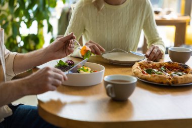 Arkadaşlar restoranda birlikte yemek yiyorlar salata ve pizza tadıyorlar içeride mutlu bir şekilde vakit geçiriyorlar.