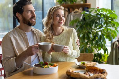 Sakallı adam ve kadın restoranda birlikte yemek yiyorlar. Tahta masada oturuyorlar. Sıcak bir ortamda pizza ve kahveyle.