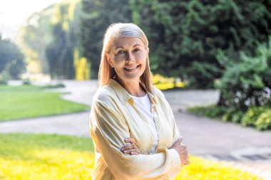 Yaşlı kadın, güpegündüz ağaçların arkasında güvenle poz veriyor.