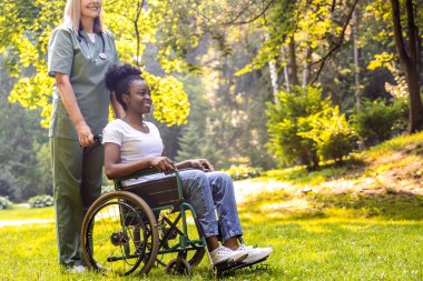 Park ortamında güneş ışığı alan rehabilitasyon egzersizinde yaşlıları destekleyen bakıcı