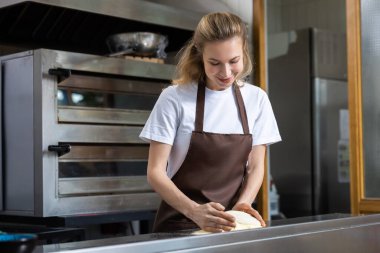 Hamur yoğuruyorum. Önlüklü genç kadın pizza pişirmek için hamur yoğuruyor.