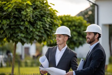 Mühendisler, ağaçlar ve güneş ışığıyla donatılmış yeşil bir ortamda projeyi planlar ve dizüstü bilgisayarlarla koordine ediyorlar.