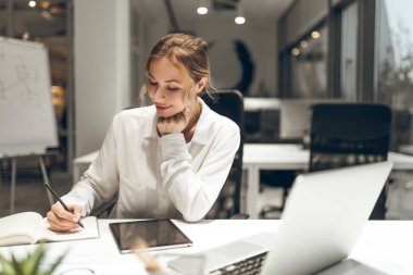 İş kadını not defterinde beyaz tahtayla birlikte çağdaş ofis ayarlarında görünür notlar alıyor