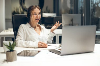 Ofis çalışanı, yeşil kulaklıklı parlak odada dizüstü bilgisayardaki görevleri yönetiyor.
