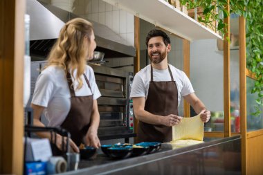 Kahverengi önlüklü kadın ve erkek restoran mutfağında pizza hamuru hazırlıyorlar.