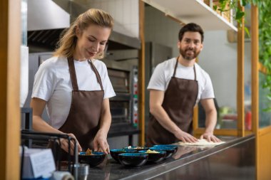 Kahverengi önlüklü kadın ve erkek restoran mutfağında pizza hamuru hazırlıyorlar.