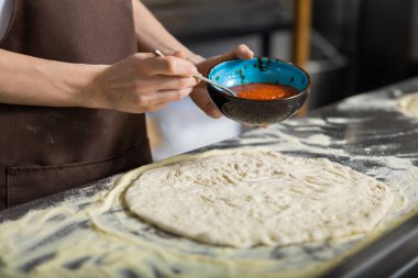 Kadın soslu pizza mutfağını dağıtıyor ve içeride dikkatlice yemek yapıyor.