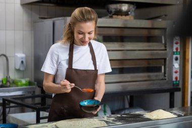 Mutfakta gülümseyen ve sos dağıtan kadın içeride yemek pişirmenin tadını çıkarıyor.