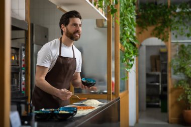 Adam mutfakta pizza hazırlıyor, sosu yayıyor dikkatlice içeride yemek yapıyor.