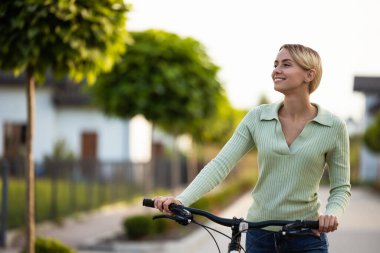 Bisikletli kadın yeşil ağaçlarla banliyöde gezmeye hazır.