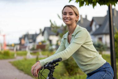 Bisikletli kadın yeşil ağaçlarla banliyöde gezmeye hazır.