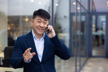 İletişim. Elinde telefon olan takım elbiseli genç Asyalı adam.